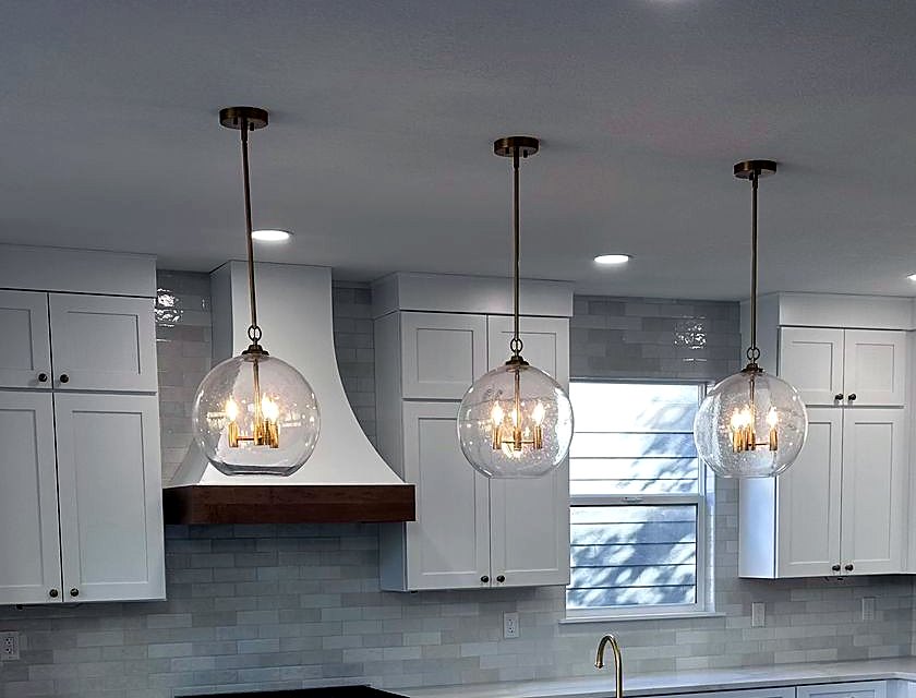 Glass pendant lights above a renovated kitchen island with white cabinetry and tile backsplash